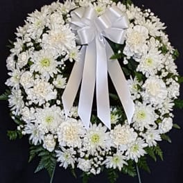 White floral funeral wreath with a satin bow on a dark background