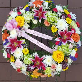 Heart-shaped floral wreath with pink lilies and mixed blooms on a stand
