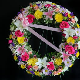 Circular floral wreath with pink ribbon and mixed blooms on a stand