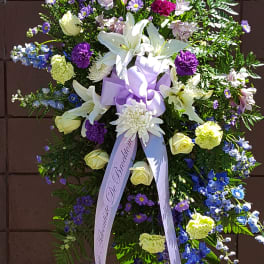 Standing floral spray with white lilies, purple and blue flowers, and a lavender ribbon