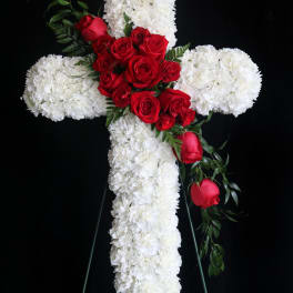 White floral cross with red roses on a black stand