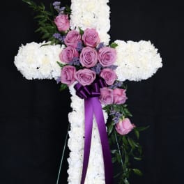 White floral cross with pink roses and a purple ribbon on an easel