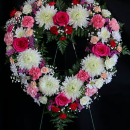 Heart-shaped floral wreath with pink roses and white chrysanthemums on a black stand