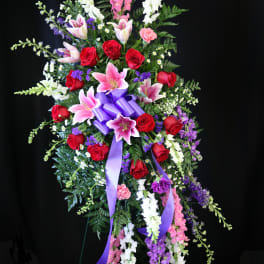 Standing floral spray with red roses, pink lilies, and purple ribbon