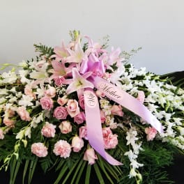 Pink lilies and roses arranged with white orchids and ribbons