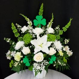 White floral arrangement with lilies, roses, and green shamrock picks in a white vase