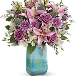 Pink lilies and roses arranged in a blue glass vase