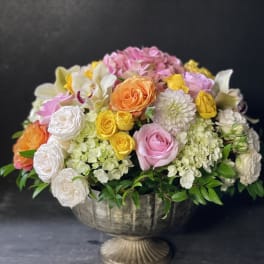 Mixed bouquet of roses, hydrangeas, and orchids in a pedestal bowl