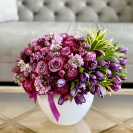Pink and purple flower arrangement in a white vase with a ribbon