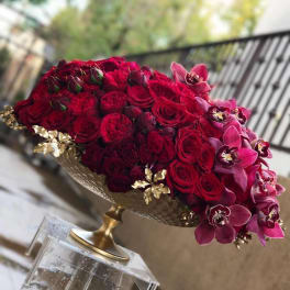 Red rose arrangement with pink orchids in a gold pedestal bowl
