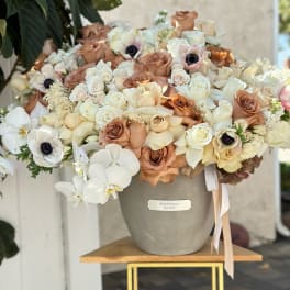 Large bouquet of cream and tan roses with white orchids in a gray vase