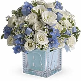 White roses and blue flowers in a glass cube vase with a monogram