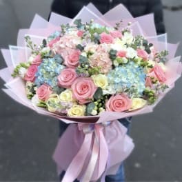 Large pastel bouquet of pink and cream roses with blue hydrangeas wrapped in pink paper and ribbon
