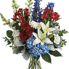 Bouquet of red roses, white lilies, blue flowers, and red alstroemeria in a glass vase