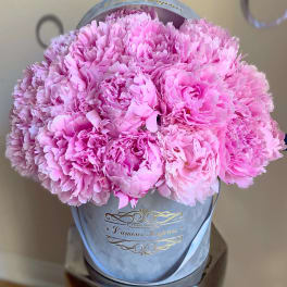 Pink peonies arranged in a gray hat box with a ribbon.