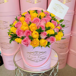 Round pink hatbox filled with pink and yellow roses and a card on a mirrored table
