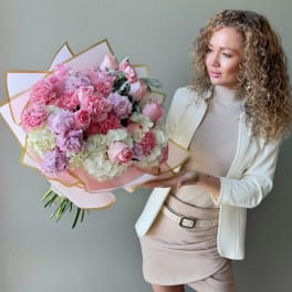 Large pink and white bouquet with roses and carnations held by a woman in a cream outfit