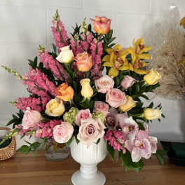 Mixed bouquet of pink, yellow, and peach flowers in a white vase.