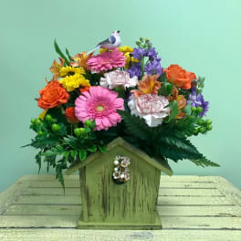 Colorful mixed flower arrangement in a small wooden birdhouse container