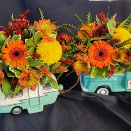 Two floral arrangements in turquoise truck containers with orange and yellow blooms
