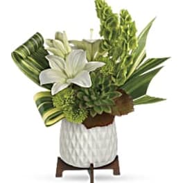 Compact white and green arrangement with lilies, succulents, and tall blooms in a white pot on a wooden stand
