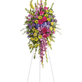 Tall standing floral spray on a white easel with pink, yellow, and purple flowers.