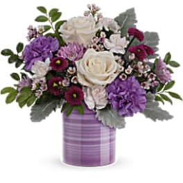 Lavender and white mixed flower arrangement with roses and carnations in a purple striped ceramic vase