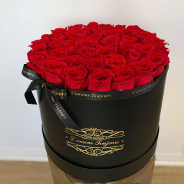 Round box filled with red roses and tied with a black ribbon