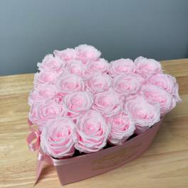 Heart-shaped pink box filled with light pink roses on a wooden surface