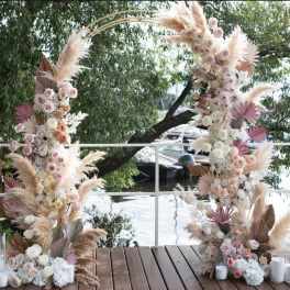 Tall floral arch with pastel roses and pampas grass beside white candles