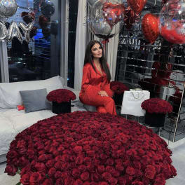 Large dome of red roses with boxed roses and heart balloons in a modern room.