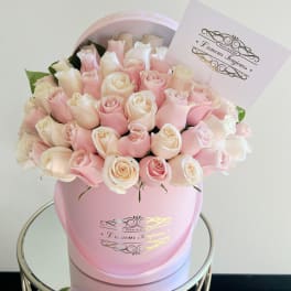 Round box of pale pink and cream roses with a card on a mirrored side table