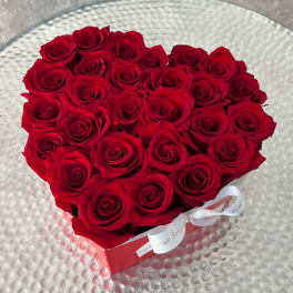 Heart-shaped box filled with red roses and tied with a white ribbon on a glass table