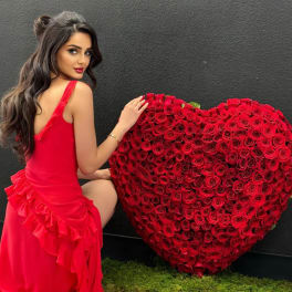 Woman in a red dress posing beside a large heart-shaped rose arrangement