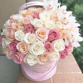 Round box of cream, blush, and pink roses with a few pale orchids in a pink hatbox