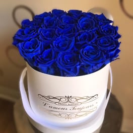 Blue roses arranged in a white round hatbox with ribbon handles