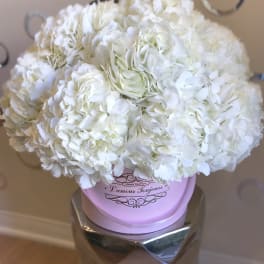 Round arrangement of white hydrangeas in a pink hat box on a metallic pedestal.