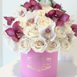 Round hatbox arrangement of cream roses and pink-purple orchids in a pink container