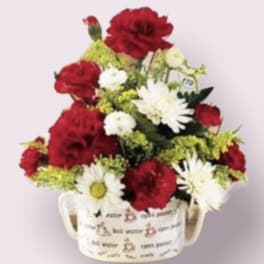 Red and white flowers arranged in a handled mug