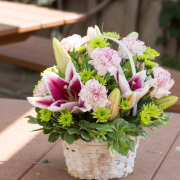 Basket arrangement of pink carnations, lilies, and green mums