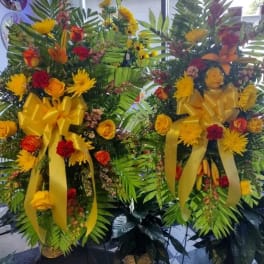 Two large floral standing sprays with yellow ribbons and mixed blooms