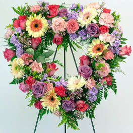 Heart-shaped floral wreath on a stand with pink, purple, and yellow blooms