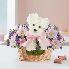 White teddy bear in a wicker basket surrounded by pink and purple flowers