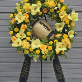 Yellow floral wreath with a gold football centerpiece on a stand