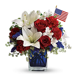 Red roses and white lilies in a blue glass vase with a small American flag