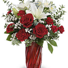 Tall red and white arrangement with roses, carnations, and lilies in a red glass vase