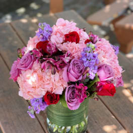 Pink and purple bouquet in a glass vase with red roses