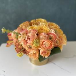 Round bouquet of peach and yellow flowers in a gold vase
