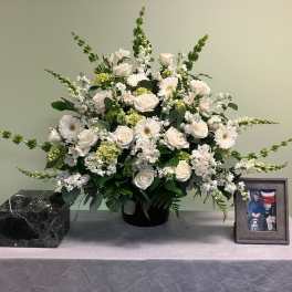 White floral arrangement in a black vase on a table with a framed photo