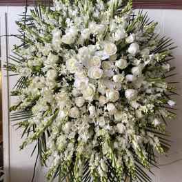 Large white funeral spray with roses and orchids on a standing easel